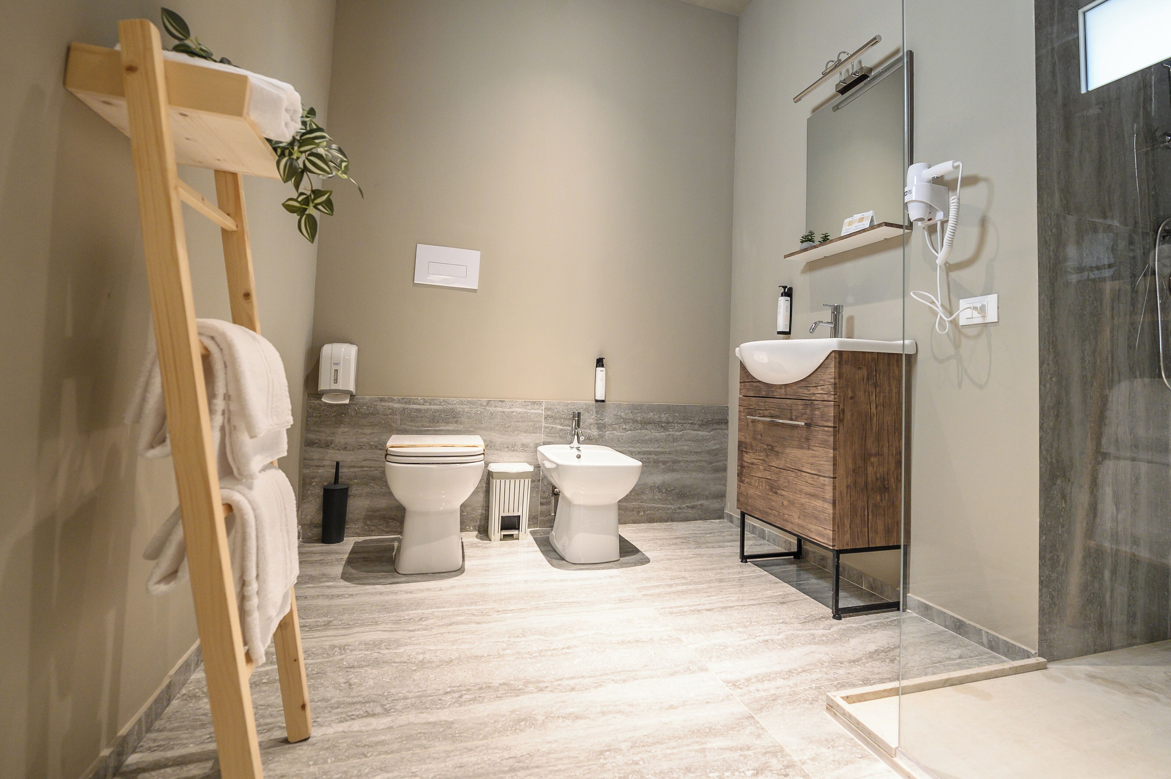 A modern bathroom with a wooden towel rack, two toilets, a bidet, a sink, and a glass shower enclosure.