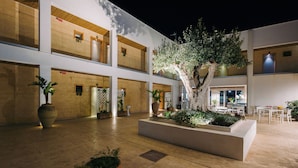 A spacious courtyard with a central tree, multiple balconies, and a seating area. - Baitan Hotel (Marsala)
