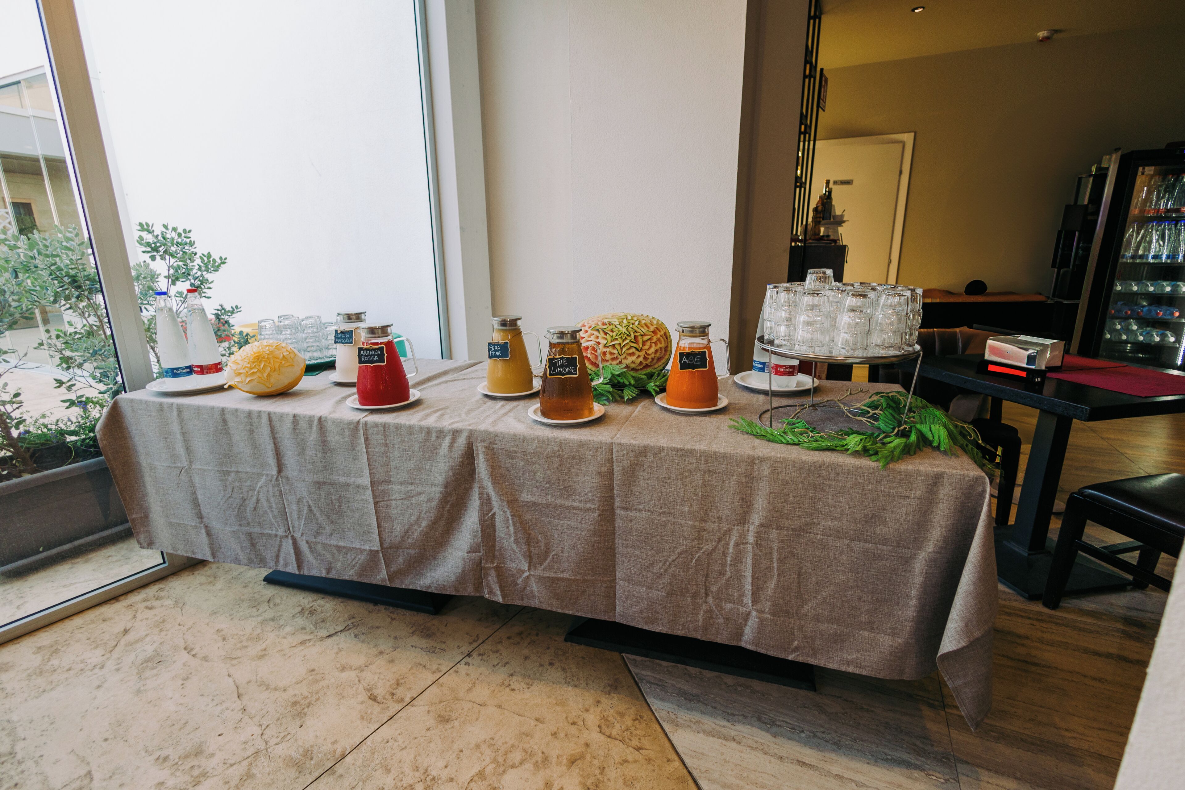 A breakfast buffet table with various food and drink options, including a pineapple, jars of sauces, and a fruit salad.