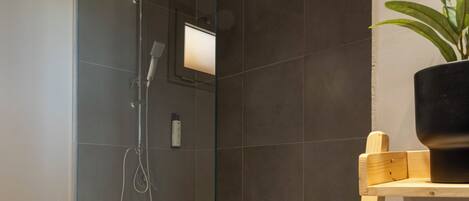 Un baño moderno con ducha de vidrio, estante de madera con planta en maceta y toalla blanca en un perchero.