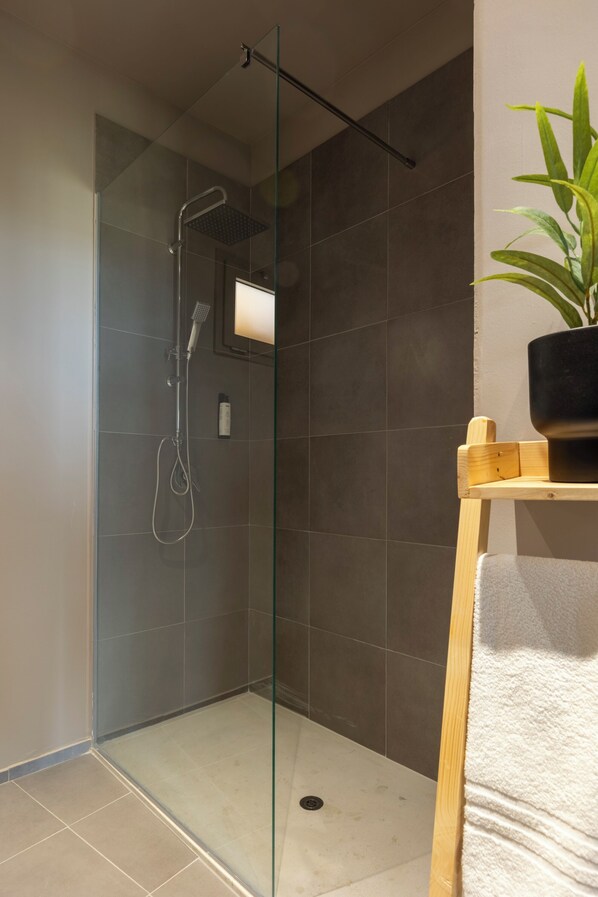 A modern bathroom with a glass-enclosed shower, a wooden shelf with a potted plant, and a white towel on a rack.