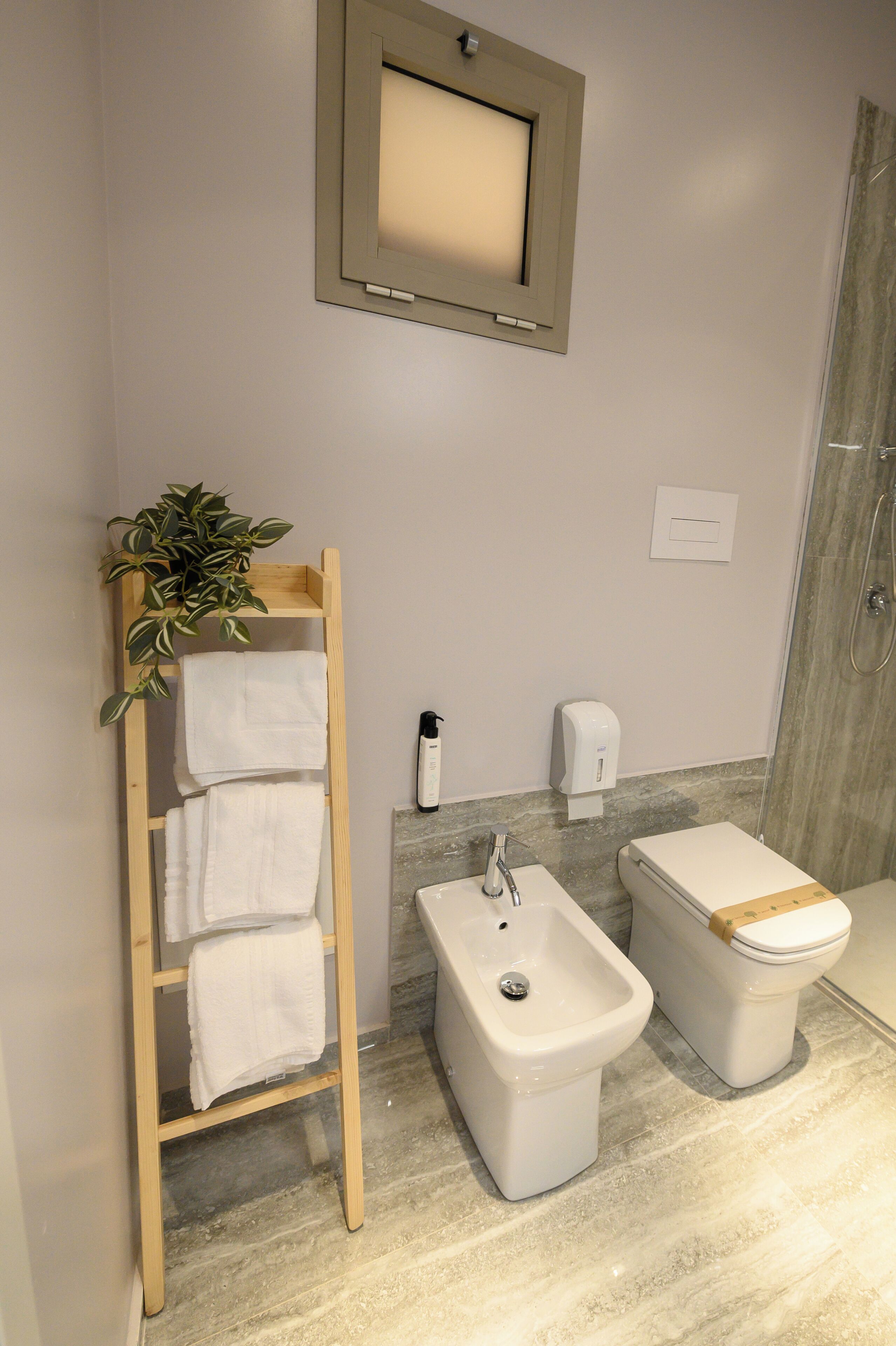Un baño con un perchero de madera, un bidé, un inodoro y una lámpara de pared.