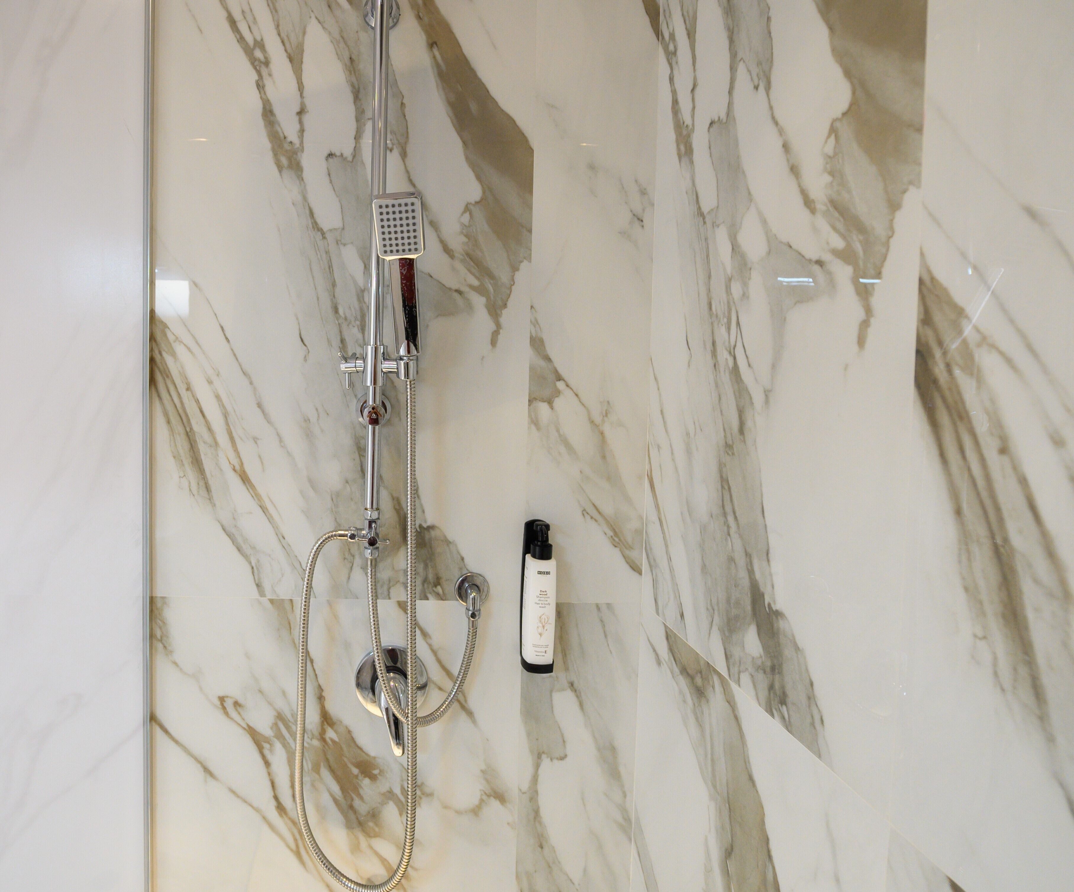 Ein Badezimmer mit Marmor und einer Dusche, inklusive Duschbrause und einer Shampooflasche.