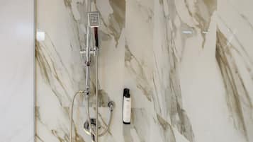Ein Badezimmer mit Marmor und einer Dusche, inklusive Duschbrause und einer Shampooflasche.
