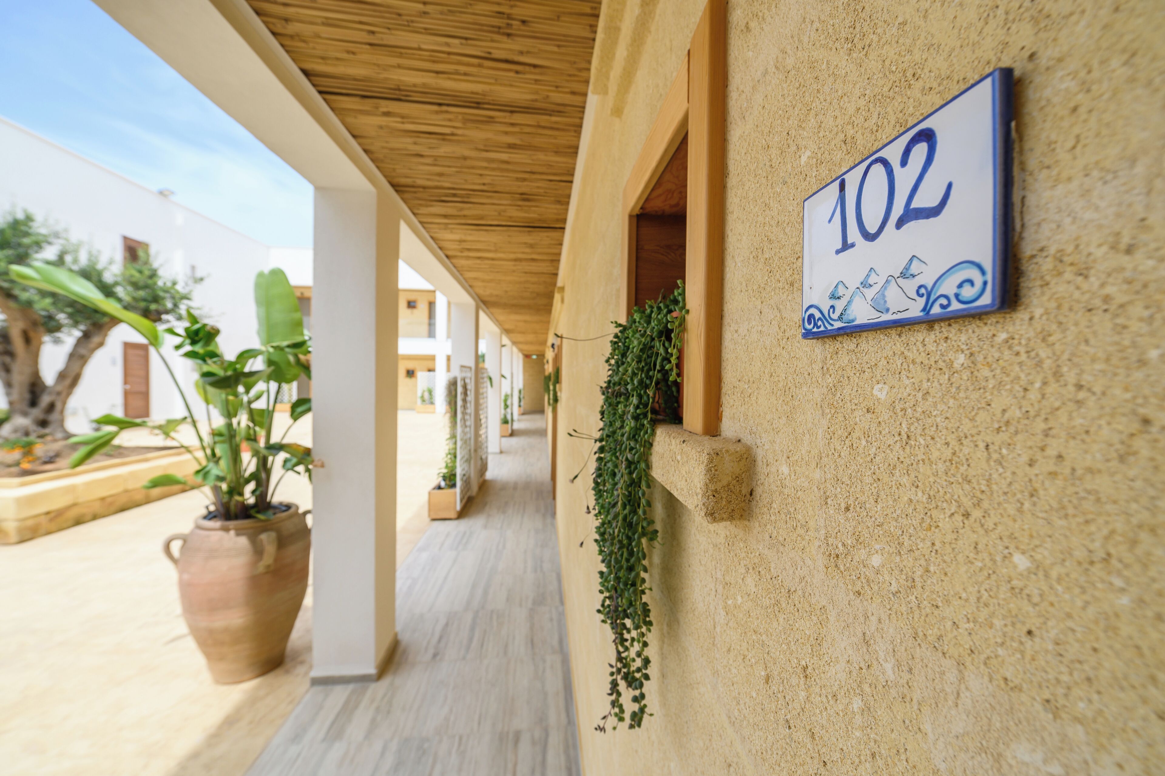 A corridor with a number sign, potted plants, and a wooden ceiling.