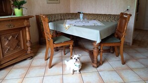 A dining area with a table set for two, surrounded by wooden chairs, a cabinet with a plant, and a wall-mounted shelf with cups. - Erholen, Entspannen, Genießen und Entdecken Eine Oase der Ruhe im Westerwald (Goddert)