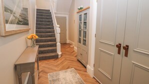 Um corredor com piso de madeira, um tapete, uma escada, um armário e uma porta.