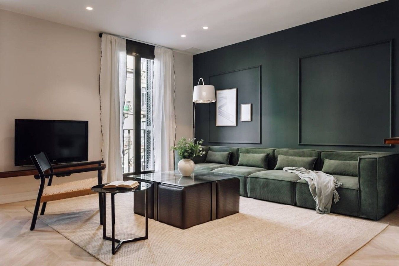 Una sala moderna con un sofá verde oscuro, un televisor de pantalla plana, una mesa de centro y una estantería.