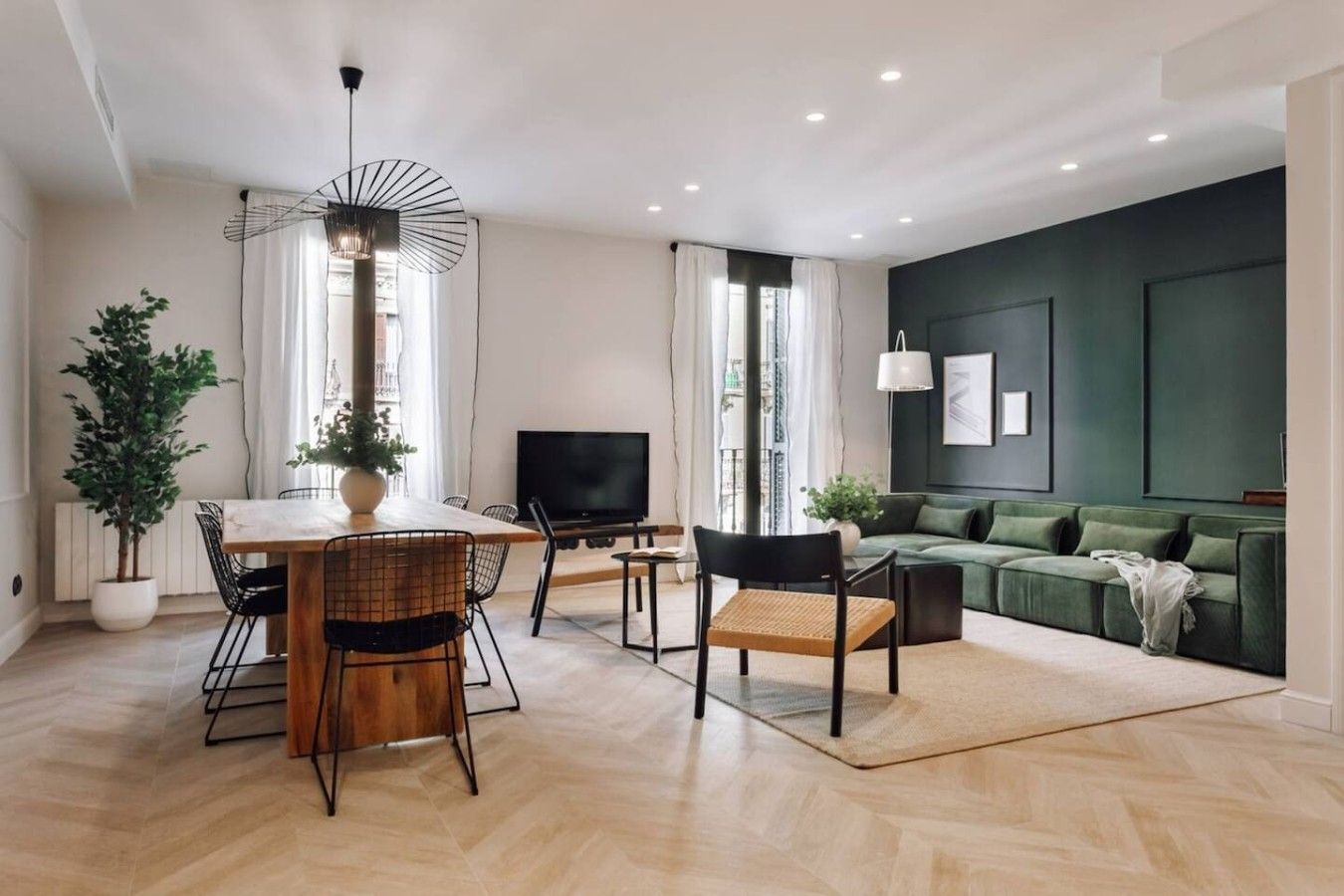A modern living room with a dining area, a green sofa, a TV, and a potted plant.