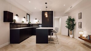 A modern kitchen with black cabinetry, a central island, and bar stools. - Lunalux - Habitat Apartments (Barcelona)