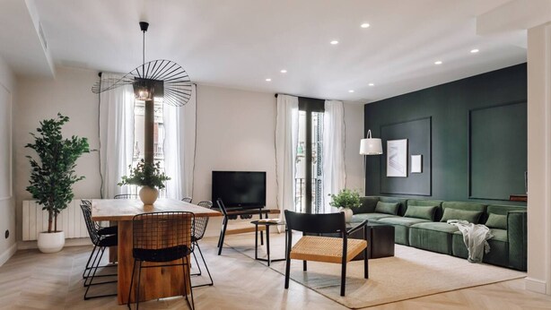 A modern living room with a dining area, a green sofa, a TV, and a potted plant. - Lunalux - Habitat Apartments (Barcelona)