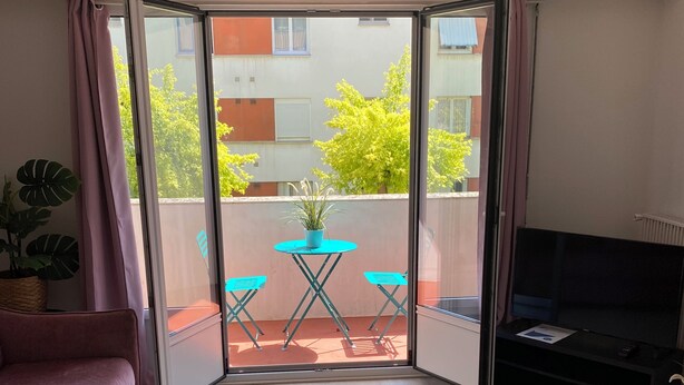 Une pièce dotée d’une porte-fenêtre coulissante donnant sur un espace extérieur aménagé avec une table et des chaises, un canapé et un téléviseur posé sur un meuble.