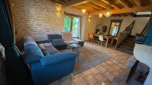 A cozy living room with a stone wall, a blue sofa, a dining table, and a staircase. - La Ferme Tchoukar, Ferme Dauphinoise à 10min du lac à Pied (BILIEU)