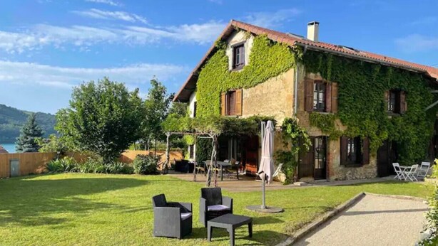 A house with ivy-covered walls, a patio with outdoor furniture, and a view of the surrounding landscape. - La Ferme Tchoukar, Ferme Dauphinoise à 10min du lac à Pied (BILIEU)