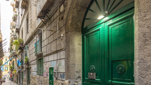 A cobblestone street with a green door and a stone archway.