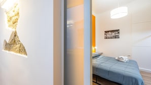 A modern bedroom with a blue bedspread, a wall-mounted light fixture, and a framed picture.
