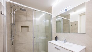 A modern bathroom with a glass-enclosed shower, a white vanity with a mirror, and a tiled floor.