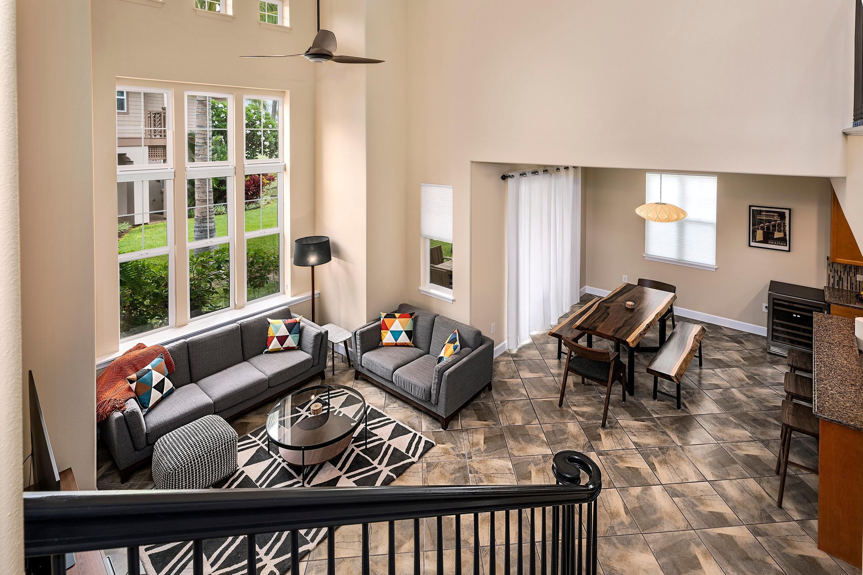 A spacious living area with a large window, a sofa set, a dining table, and a staircase.
