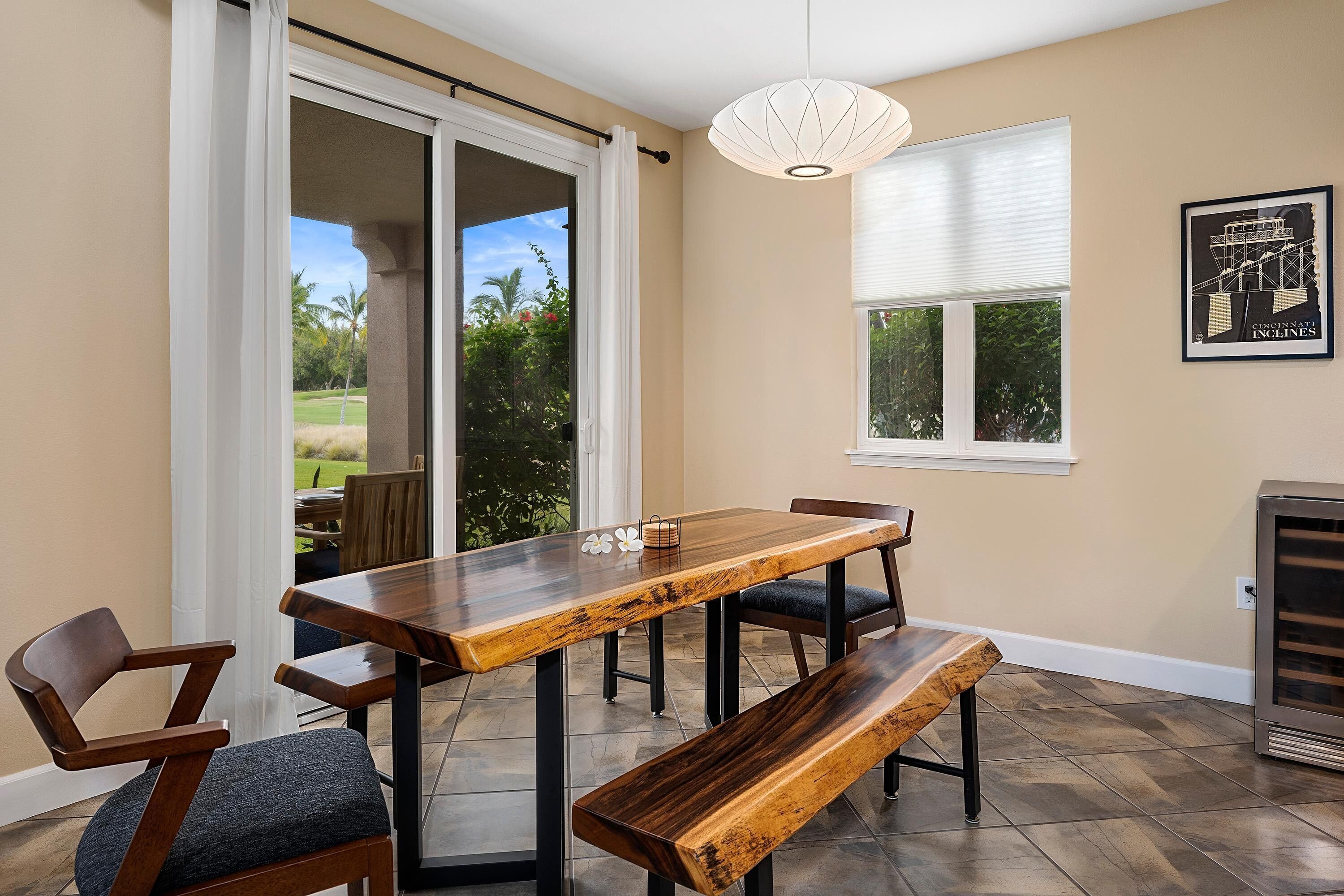 Un comedor con mesa y bancos de madera, un ventanal corredero que da a un patio exterior y un plano arquitectónico enmarcado en la pared.