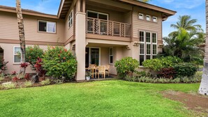 A two-story house with a balcony, surrounded by a well-maintained garden with various plants and a lawn. - Colony Villas Waikoloa 301 (Waikoloa)