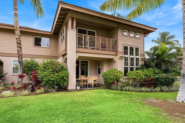 A two-story house with a balcony, surrounded by a well-maintained garden with various plants and a lawn. - Colony Villas Waikoloa 301 (Waikoloa)