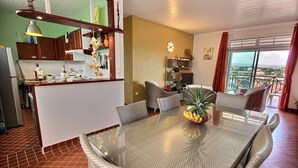 A dining area with a glass table and wicker chairs, a kitchen with wooden cabinets, and a balcony with a view. - Villa Cécia - Four Bedroom Villa, Sleeps 8 (Les Trois-Îlets)