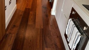 A narrow hallway with wooden flooring leading to a door, a kitchen area with a sink and cabinets, and a towel hanging on a rack. - Studio Apartment w/ Balcony In Canary Wharf (London)