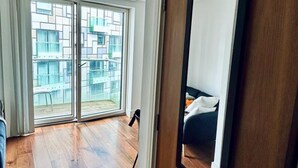 A hotel room with a wooden floor, a large sliding glass door leading to a balcony, and a wooden door with a mirror. - Studio Apartment w/ Balcony In Canary Wharf (London)