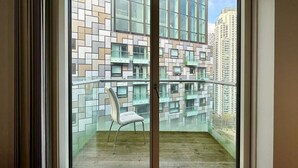 A balcony with a chair, a glass door, and a view of a modern building with multiple windows. - Studio Apartment w/ Balcony In Canary Wharf (London)