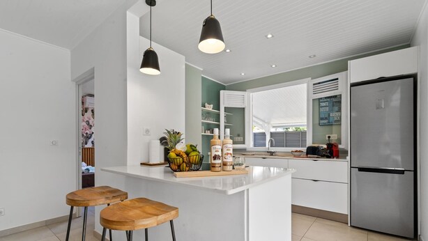A modern kitchen with a central island, two bar stools, a stainless steel refrigerator, and pendant lighting.