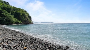A pebbled beach with a rocky shoreline and a forested cliff.