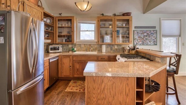 A kitchen with wooden cabinets, a stainless steel refrigerator, a granite countertop, and a hanging light fixture.