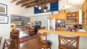A kitchen with wooden cabinets, a central island, and a dining area with wooden chairs.