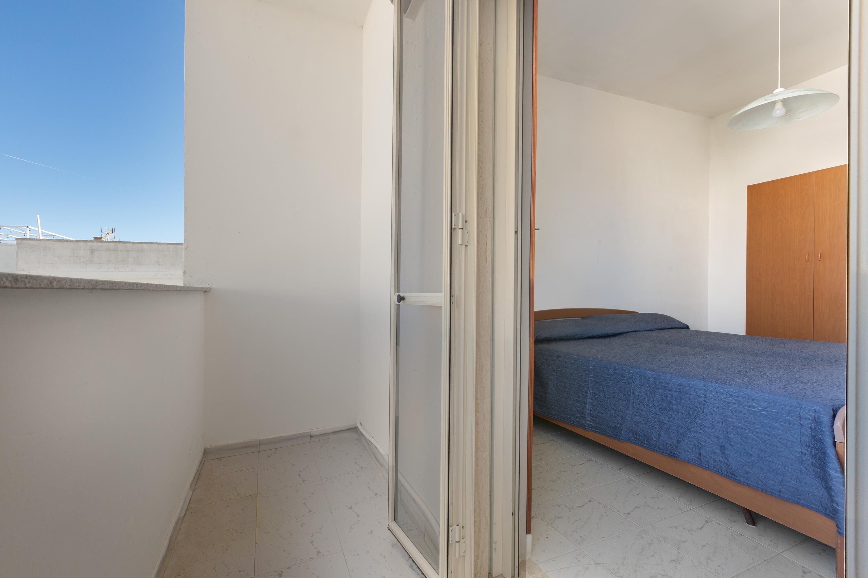 A bedroom with a bed, a wooden wardrobe, and a sliding glass door leading to an outdoor balcony.