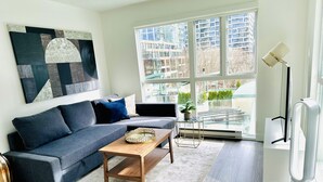 Ein modernes Wohnzimmer mit grauem Sofa, einem Holztisch und einem großen abstrakten Gemälde an der Wand.