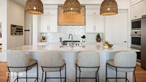 Una cucina moderna con isola centrale, mobili bianchi e tre lampade a sospensione in vimini.
