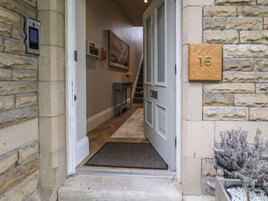 Un ingresso con pareti in pietra, una porta in legno con la scritta '16', un tappetino, un piccolo tavolo con un vaso e una scala che conduce all'interno.