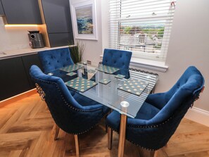 A dining area with a glass table and blue upholstered chairs. - Netherdale Penthouse (Buxton)