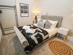 A neatly arranged bedroom with a bed, a bedside table, a lamp, a framed picture on the wall, a mirror, and a decorative rug. - Netherdale Penthouse (Buxton)