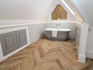 A modern bathroom with a herringbone wood floor, a freestanding bathtub, and a vanity with a mirror above it. - Netherdale Penthouse (Buxton)