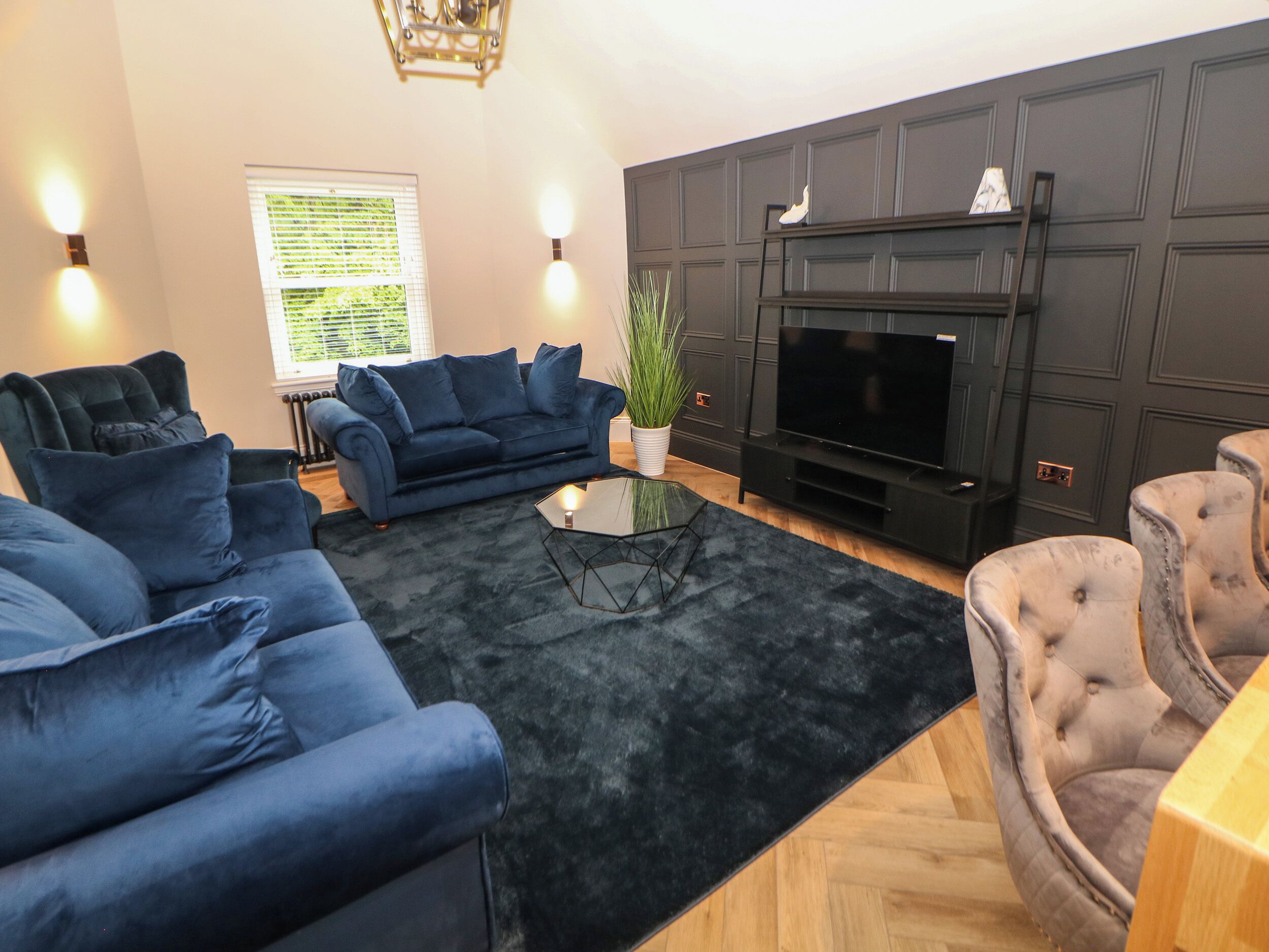 A modern living room with a sectional sofa, a glass coffee table, and a flat-screen TV against a dark wall.