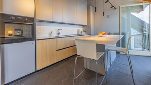 Una cocina moderna con horno empotrado, un lavamanos y una zona de comedor con mesa y taburetes de bar.