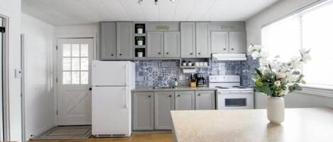 A modern kitchen with grey cabinets, a white refrigerator, a tiled backsplash, and a large window.