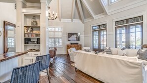 A spacious living area with a high ceiling, a dining area with a wooden table and chairs, and a cozy seating area with a sofa and cushions.