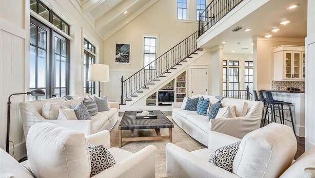 A spacious living room with high ceilings and a staircase leading to an upper level.