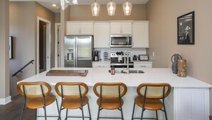 Una cocina moderna con armarios blancos, electrodomésticos de acero inoxidable y una isla central con taburetes de bar.