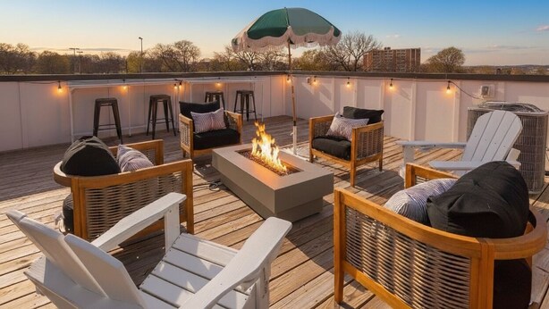 Una terraza en la azotea con mobiliario exterior, una chimenea, luces colgantes y un paraguas.