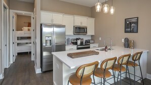 Una cocina moderna con armarios blancos, electrodomésticos de acero inoxidable y una isla central con taburetes de bar.