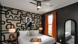 Una habitación de hotel moderna con una cama grande, un ventilador de techo, una mesita de noche con una lámpara, una bandeja con artículos de desayuno y un espejo grande.