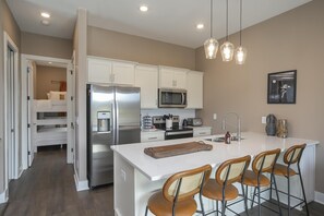 Una cocina moderna con armarios blancos, electrodomésticos de acero inoxidable y una isla central con taburetes de bar.